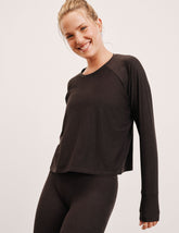 woman wearing a brown long-sleeve top and leggings on a plain background.